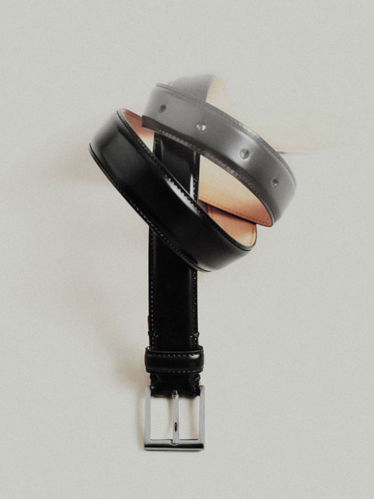 A twisted black leather belt with a shiny rectangular silver buckle, displayed against a plain light background.