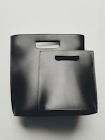 Placeholder for: Two sleek black leather bags with handle cutouts, one slightly larger than the other, on a light gray background.