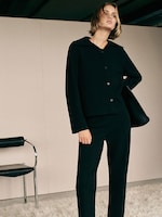 Placeholder for: Model in a black tailored outfit stands confidently in a minimalist room with a leather chair and a shaggy white rug.