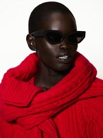 Placeholder for: Person in dark sunglasses wearing a chunky red knit sweater, exuding a bold, stylish look against a plain backdrop.