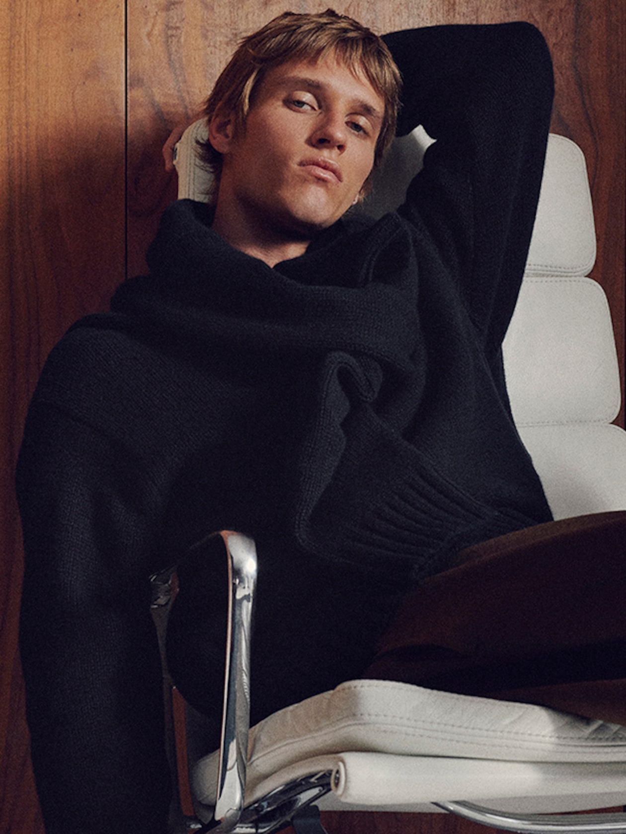 Person lounging in a white chair, wearing a black sweater. The background features a wooden surface, creating a cozy, relaxed ambiance.