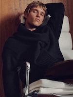 Placeholder for: Person lounging in a white chair, wearing a black sweater. The background features a wooden surface, creating a cozy, relaxed ambiance.