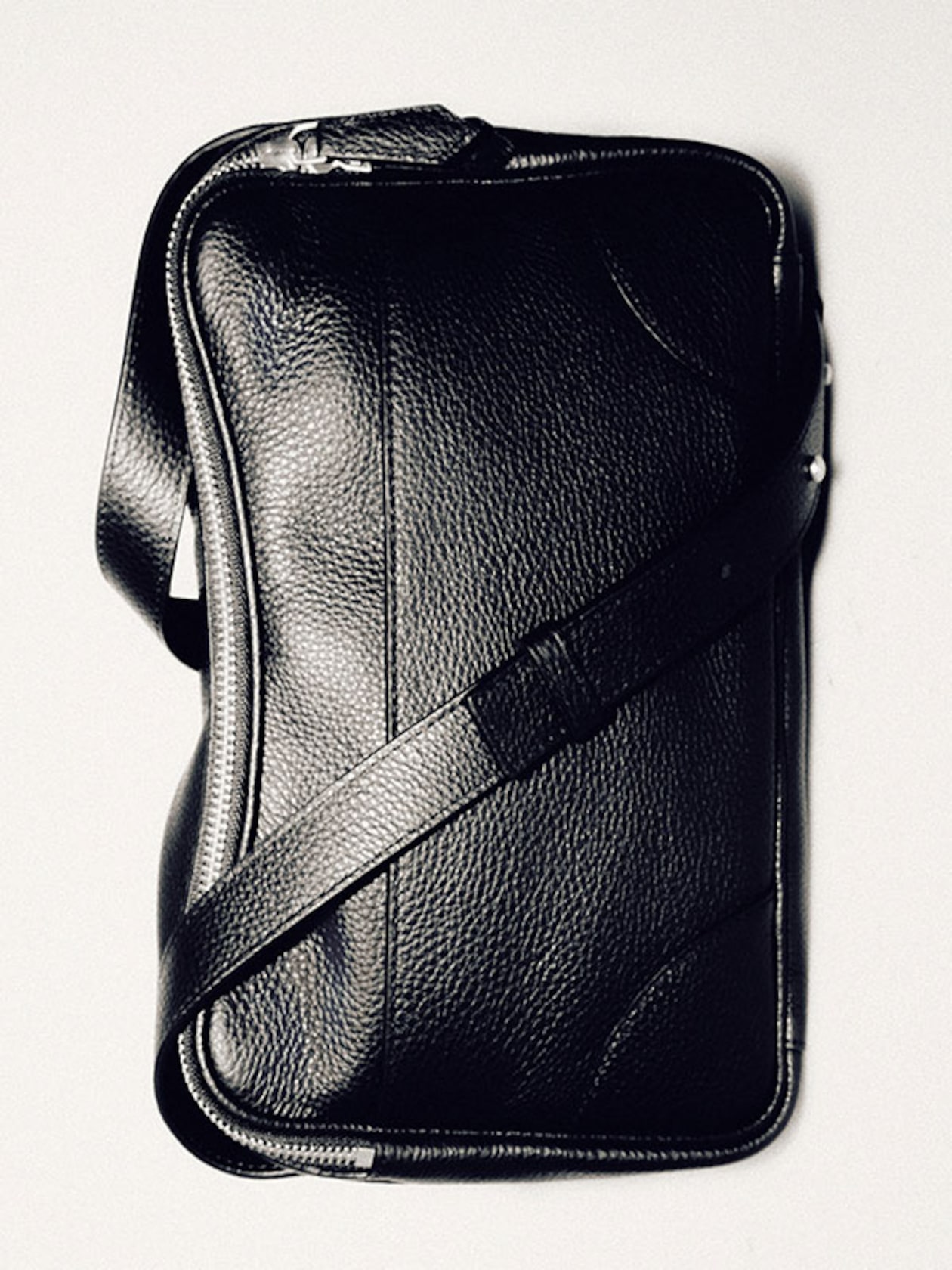 Black leather messenger bag with a textured surface and a long adjustable strap, placed against a light background.