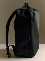Placeholder for: Minimalist black backpack with a sleek design, featuring a zipper on one side and an adjustable strap, set against a neutral background.