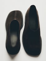 Placeholder for: Pair of dark brown suede slip-on shoes on a light background, showing top and bottom views with visible stitching and textured soles.