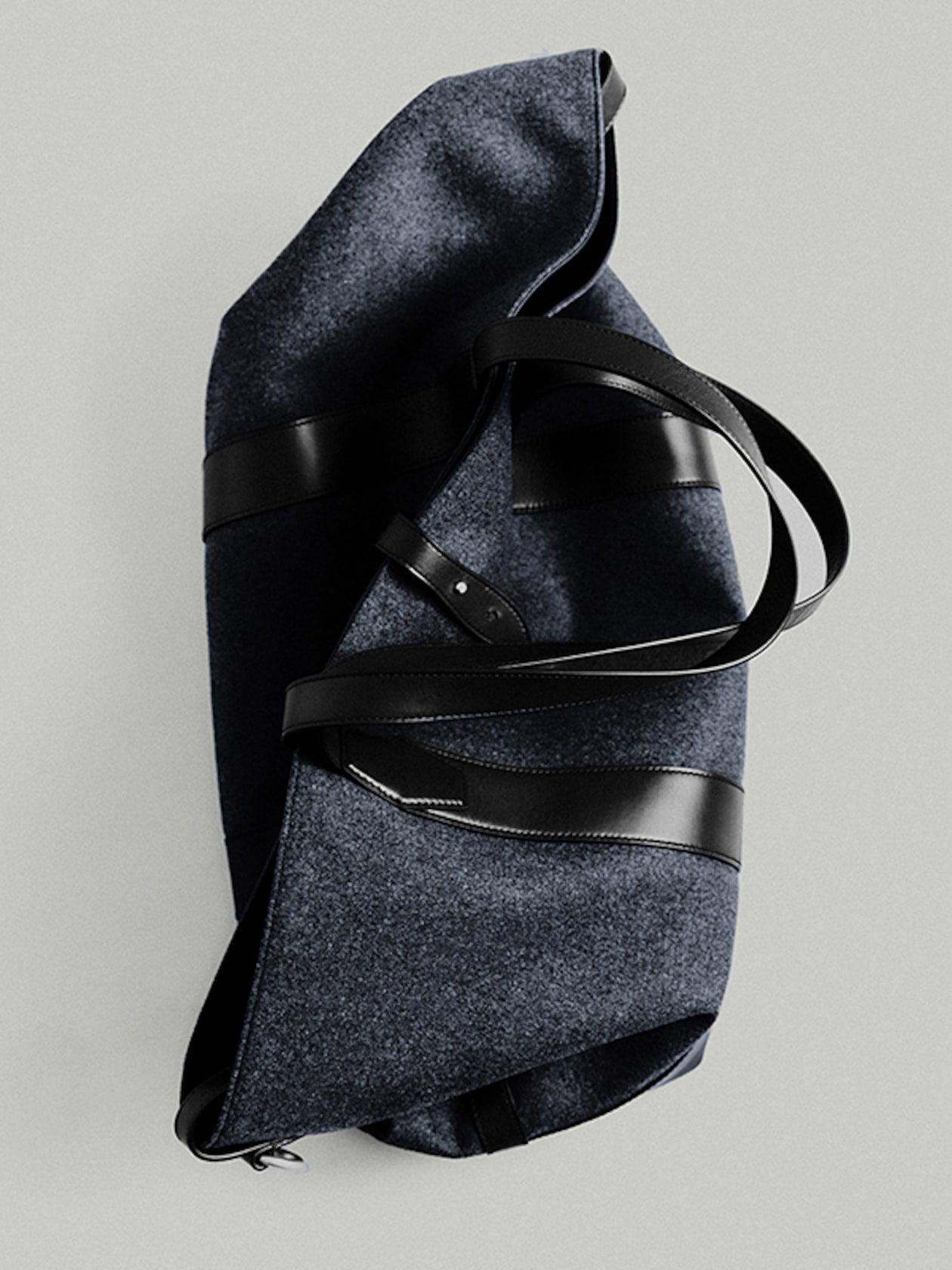A dark blue felt tote bag with black leather straps and accents, laid on a light gray background.