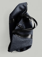 Placeholder for: A dark blue felt tote bag with black leather straps and accents, laid on a light gray background.