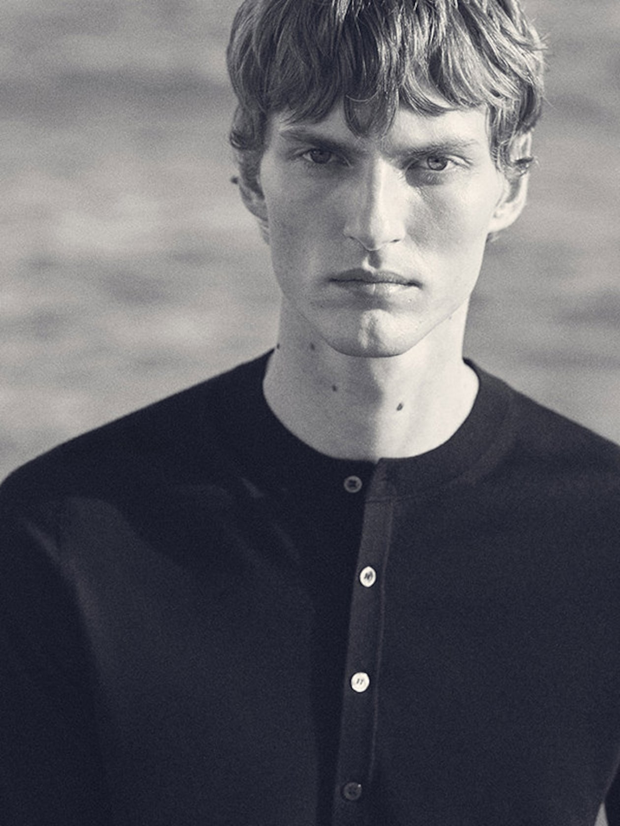 Black and white portrait of a person with short hair and a buttoned-up shirt, looking directly into the camera with a neutral expression.