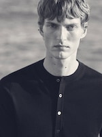 Placeholder for: Black and white portrait of a person with short hair and a buttoned-up shirt, looking directly into the camera with a neutral expression.