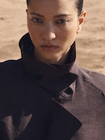 Placeholder for: Woman wearing a dark coat with a high collar, standing outdoors with a serious expression.