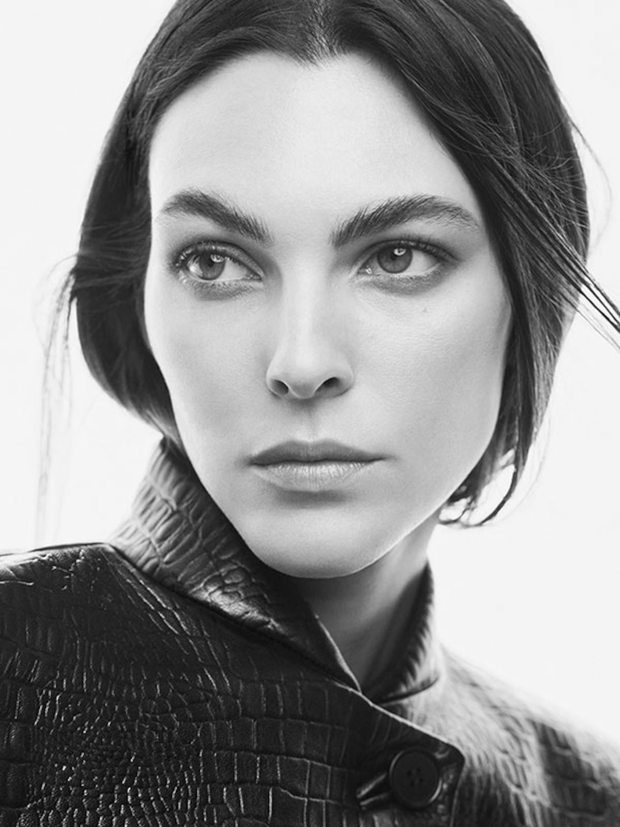 Black and white portrait of a person with dark hair, wearing a textured jacket, looking slightly to the side with a serious expression.