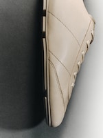Placeholder for: Beige leather sneaker viewed from the side on a two-toned background, showing details of stitching and laces.