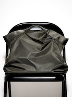 Placeholder for: A large, dark green tote bag with black handles rests against the back of a black folding chair on a white background.