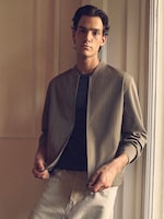 Placeholder for: Person wearing a light jacket over a dark shirt, standing in a softly lit room with a relaxed expression.