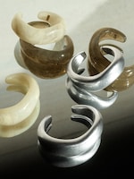 Placeholder for: Six glossy cuff bracelets in various materials and colors, including silver and earthy tones, displayed on a reflective surface.