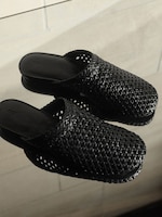 Placeholder for: Black woven slip-on shoes with a reflective surface, showcasing intricate texture and craftsmanship.