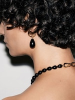 Placeholder for: Close-up of a person with curly hair wearing black teardrop earrings and a matching necklace, facing away from the camera.