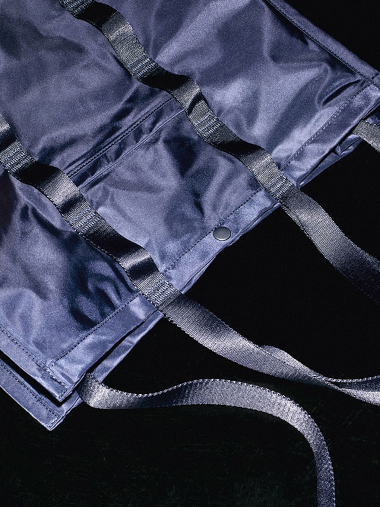 Close-up of a dark blue fabric bag with black straps and a snap button, placed on a dark surface.