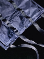 Placeholder for: Close-up of a dark blue fabric bag with black straps and a snap button, placed on a dark surface.