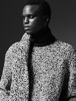 Placeholder for: Black and white portrait of a person wearing a textured knit sweater and scarf, looking thoughtfully to the side.