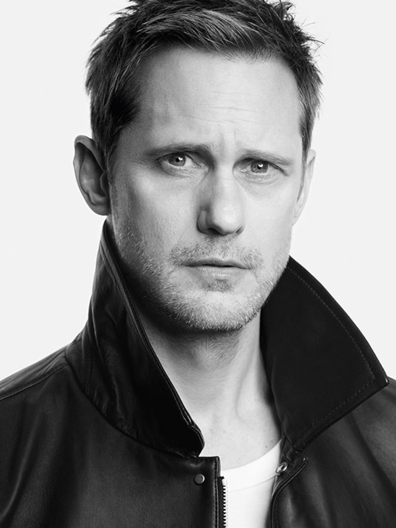 Black and white portrait of a man with short hair, wearing a leather jacket with the collar up, looking directly at the camera against a plain background.
