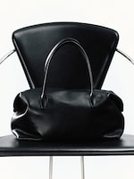 Placeholder for: A black leather handbag with handles sits on a matching black chair with a modern design.