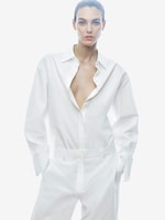Placeholder for: A person wearing a white shirt with an open collar and matching white pants, standing against a white background.