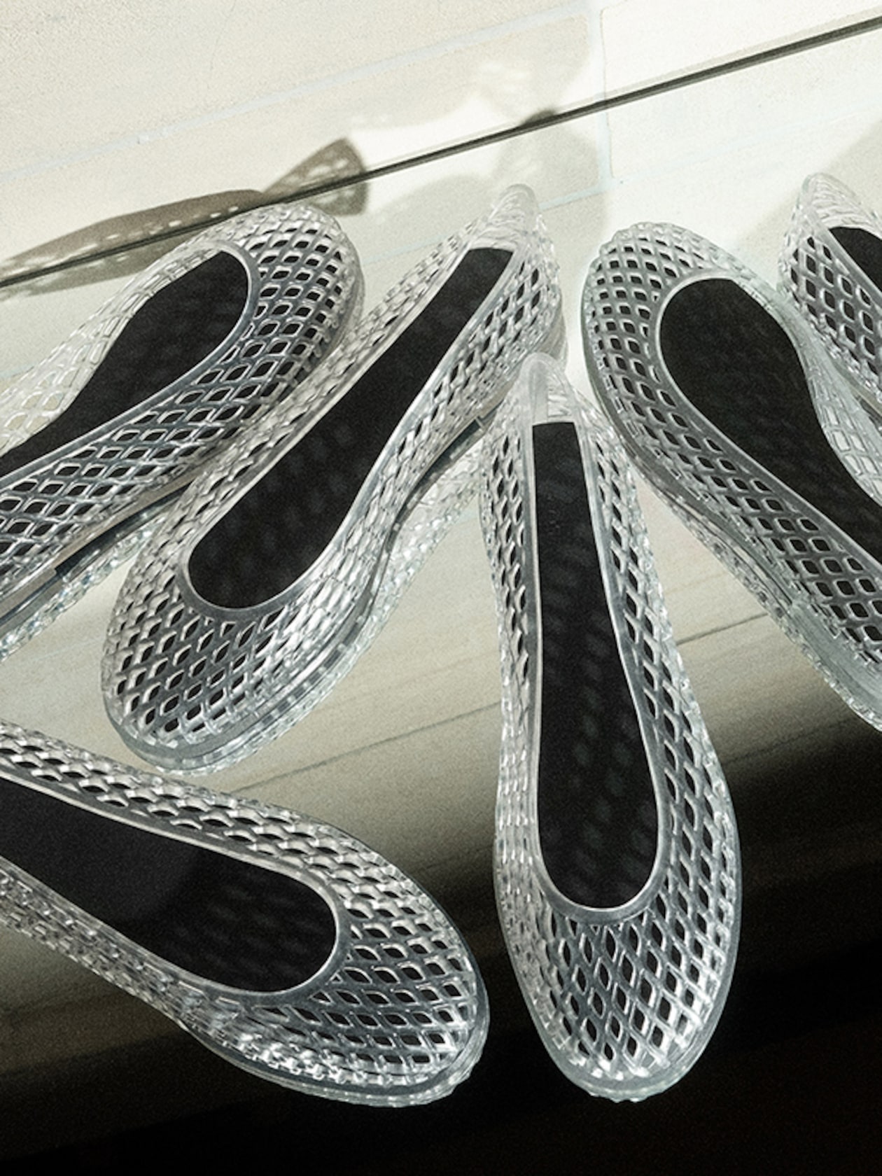 Clear mesh shoes with black insoles arranged on a reflective surface, showcasing their intricate lattice design.