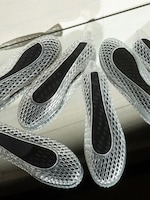 Placeholder for: Clear mesh shoes with black insoles arranged on a reflective surface, showcasing their intricate lattice design.