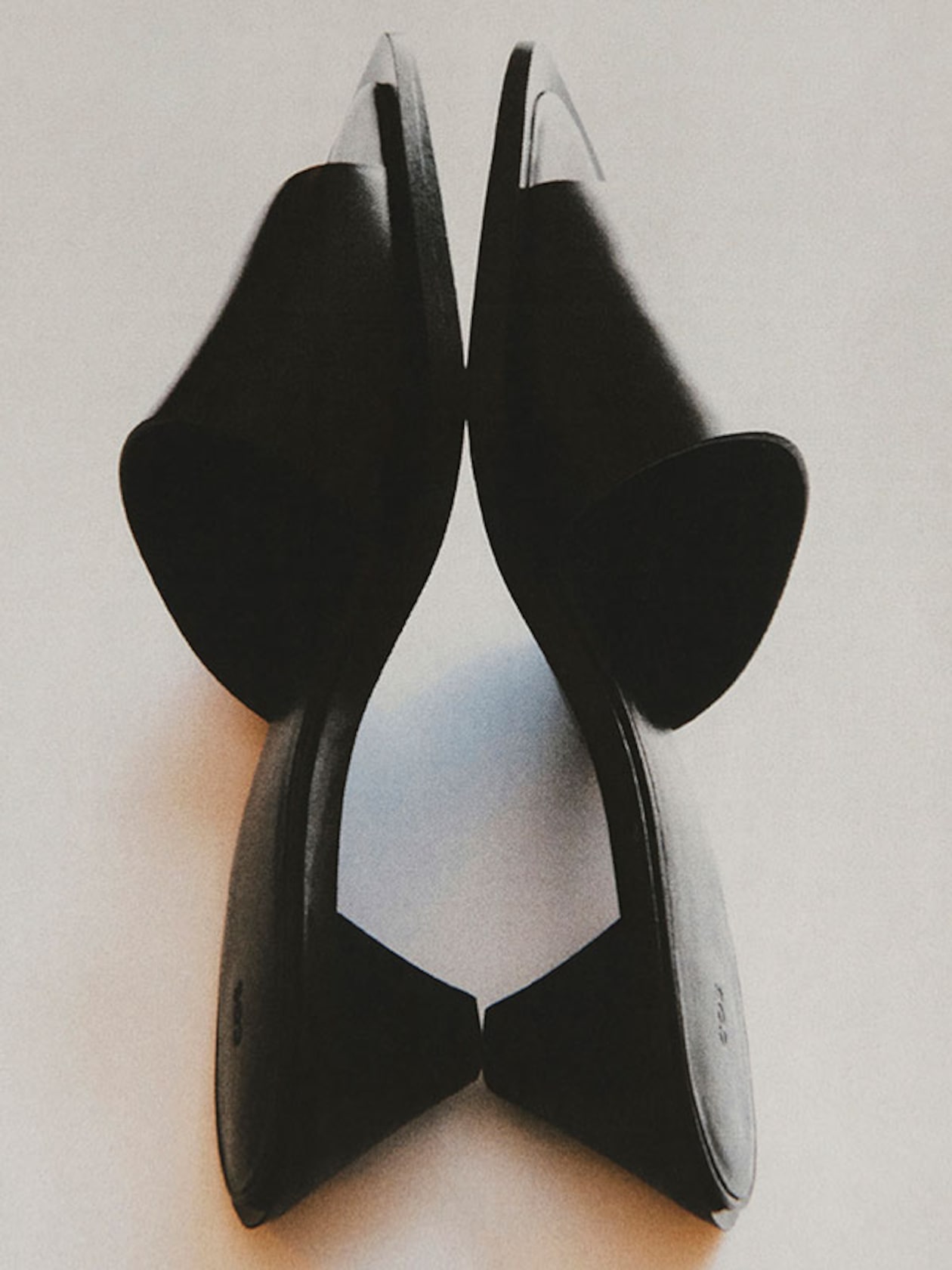 Two black shoes placed heel-to-heel on a white surface, creating a symmetrical and artistic visual.