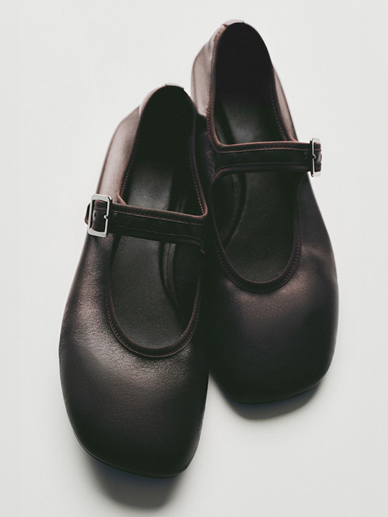 Pair of black Mary Jane shoes with buckled straps resting on a white surface.