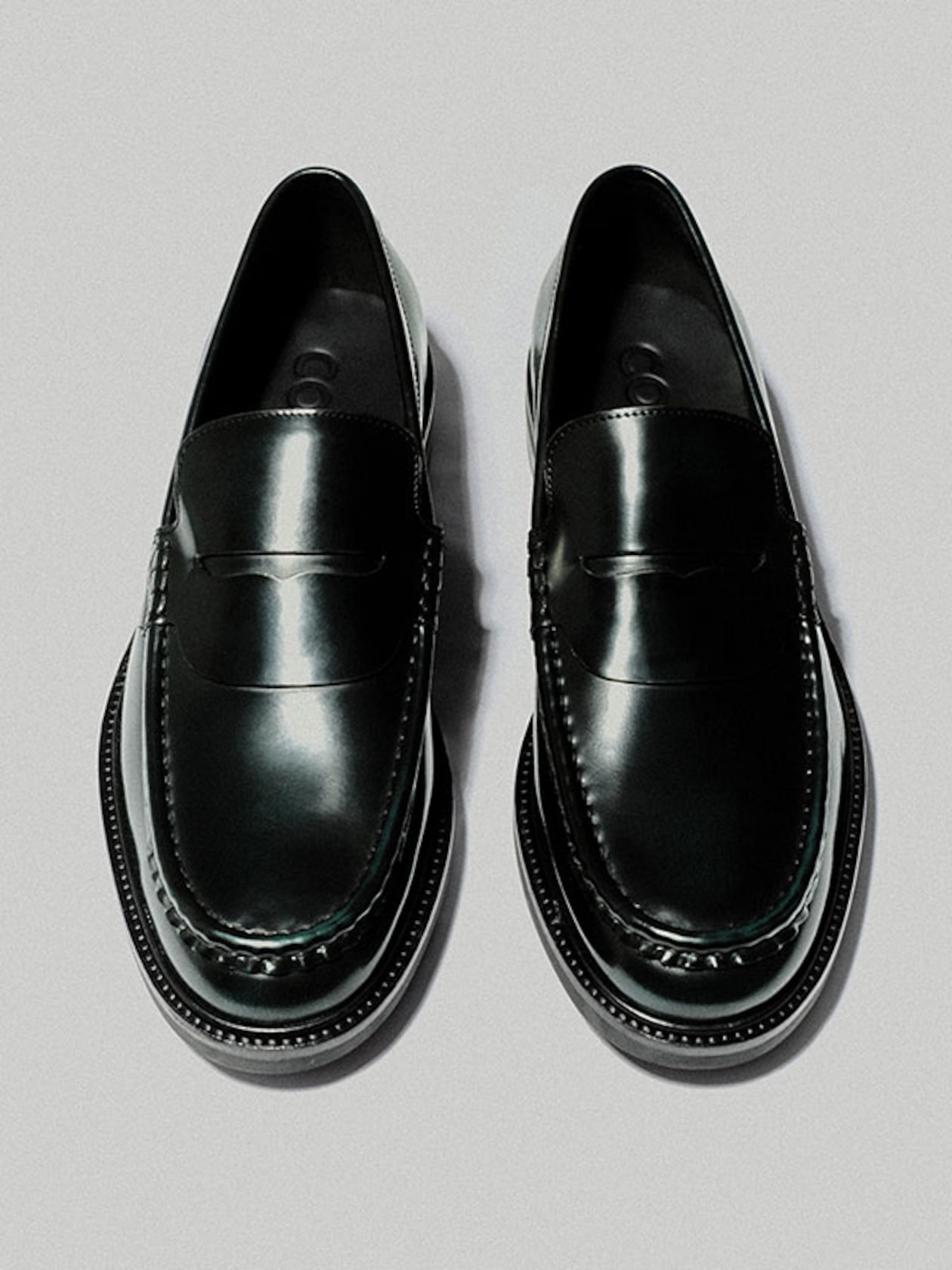 Pair of polished black leather loafers with stitching detail, viewed from above on a light gray background.