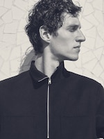 Placeholder for: Black and white photo of a person in profile wearing a dark jacket against a textured wall.