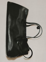 Placeholder for: Black leather tote bag with sleek design and two thin handles, lying against a neutral background.