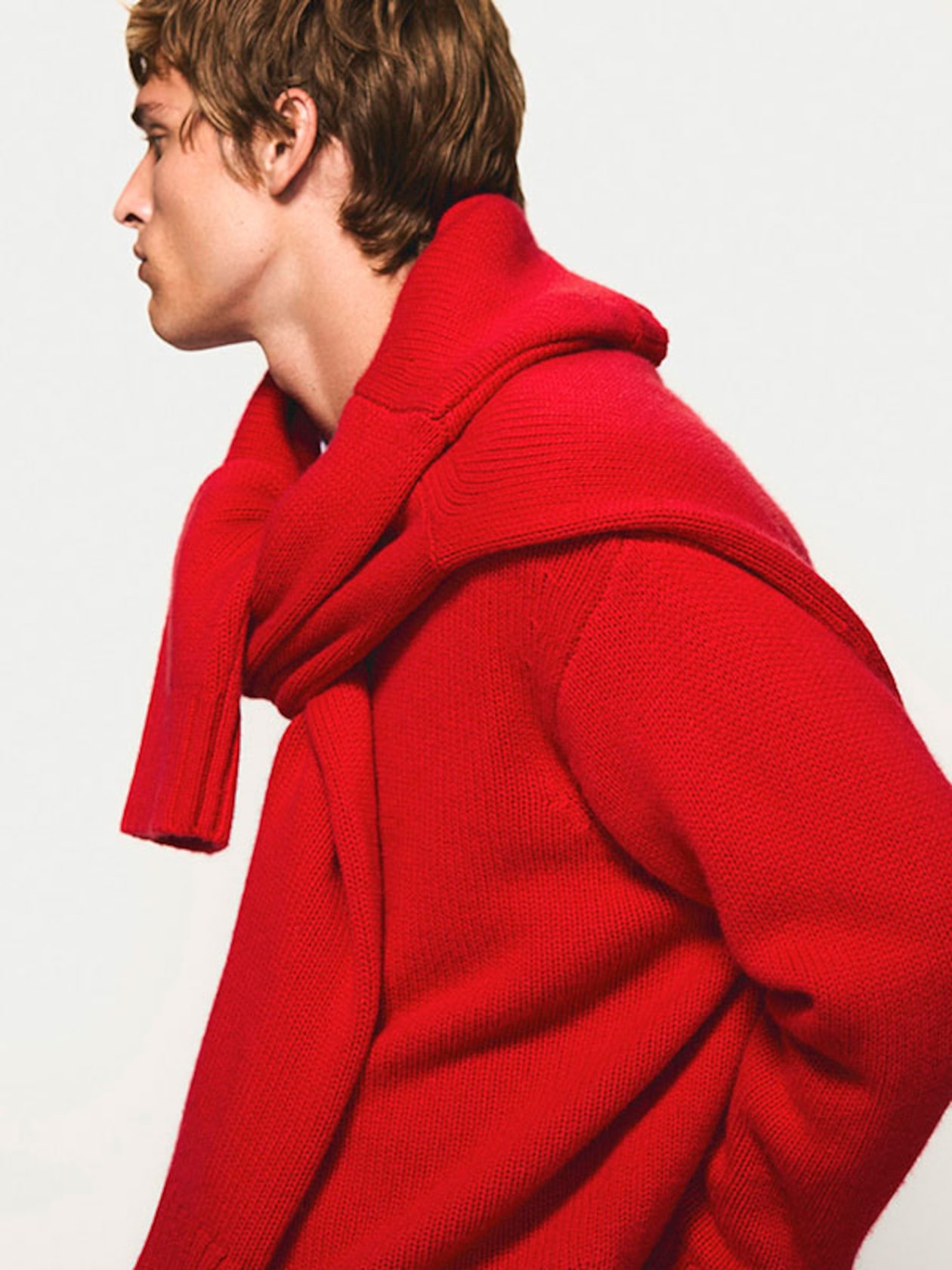 Person in profile wearing a bold red sweater with a matching garment draped over the shoulders, against a plain background.
