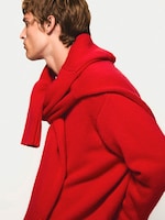 Placeholder for: Person in profile wearing a bold red sweater with a matching garment draped over the shoulders, against a plain background.