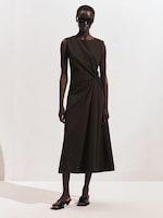 Placeholder for: A person wearing a sleeveless, dark midi dress with a twist detail, sunglasses, and black slide sandals, standing against a plain backdrop.