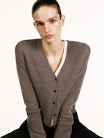 Placeholder for: Person in a gray buttoned cardigan over a white top, with slicked-back hair, looking at the camera against a plain background.