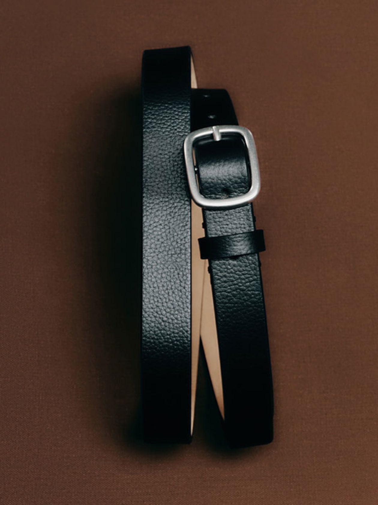 A black leather belt with a silver rectangular buckle displayed on a brown background.