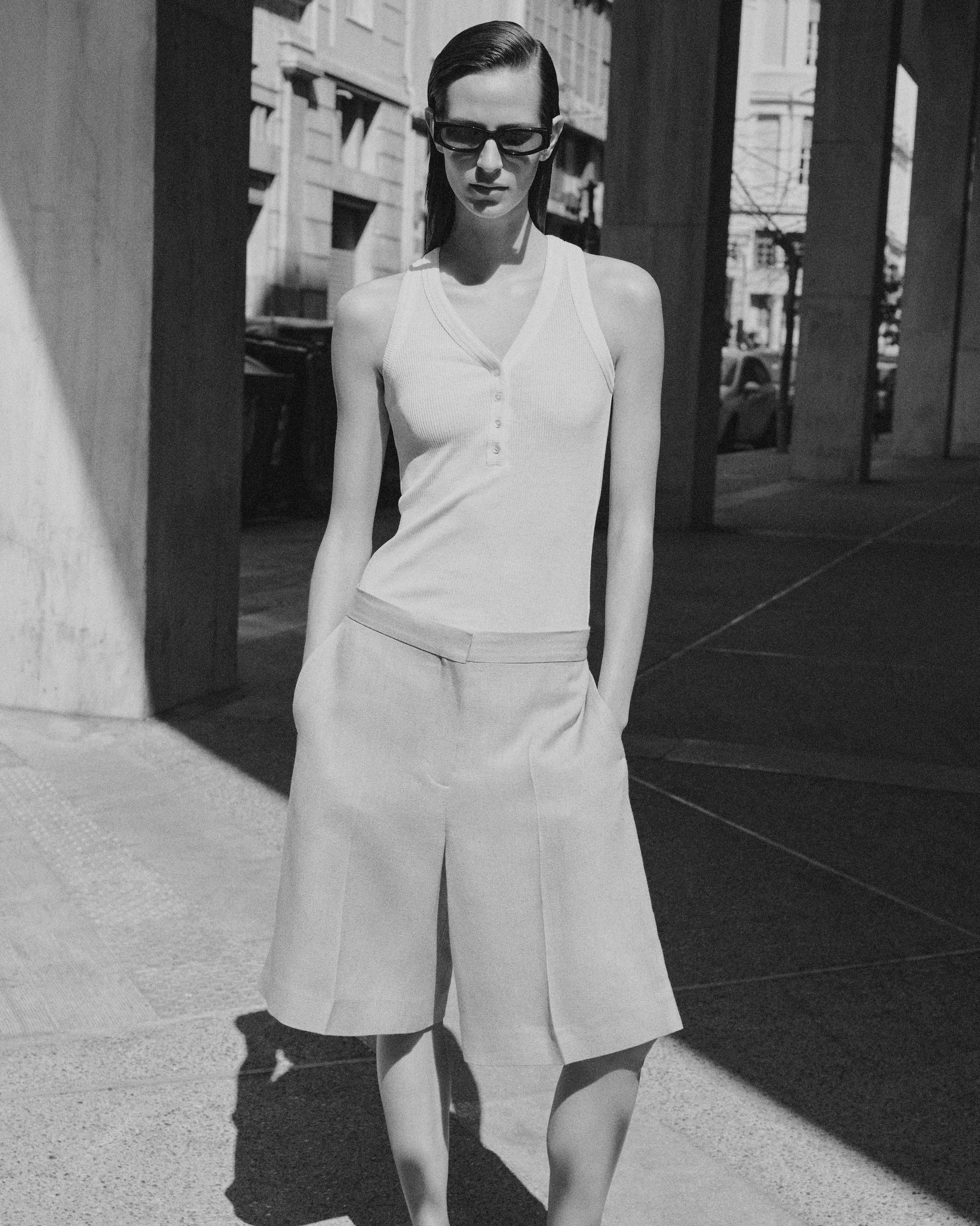 woman in tank top and shorts with sunglasses in black and white