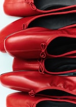 Placeholder for: Stacked red ballet flats with rounded toes and bow detailing, viewed from the side.