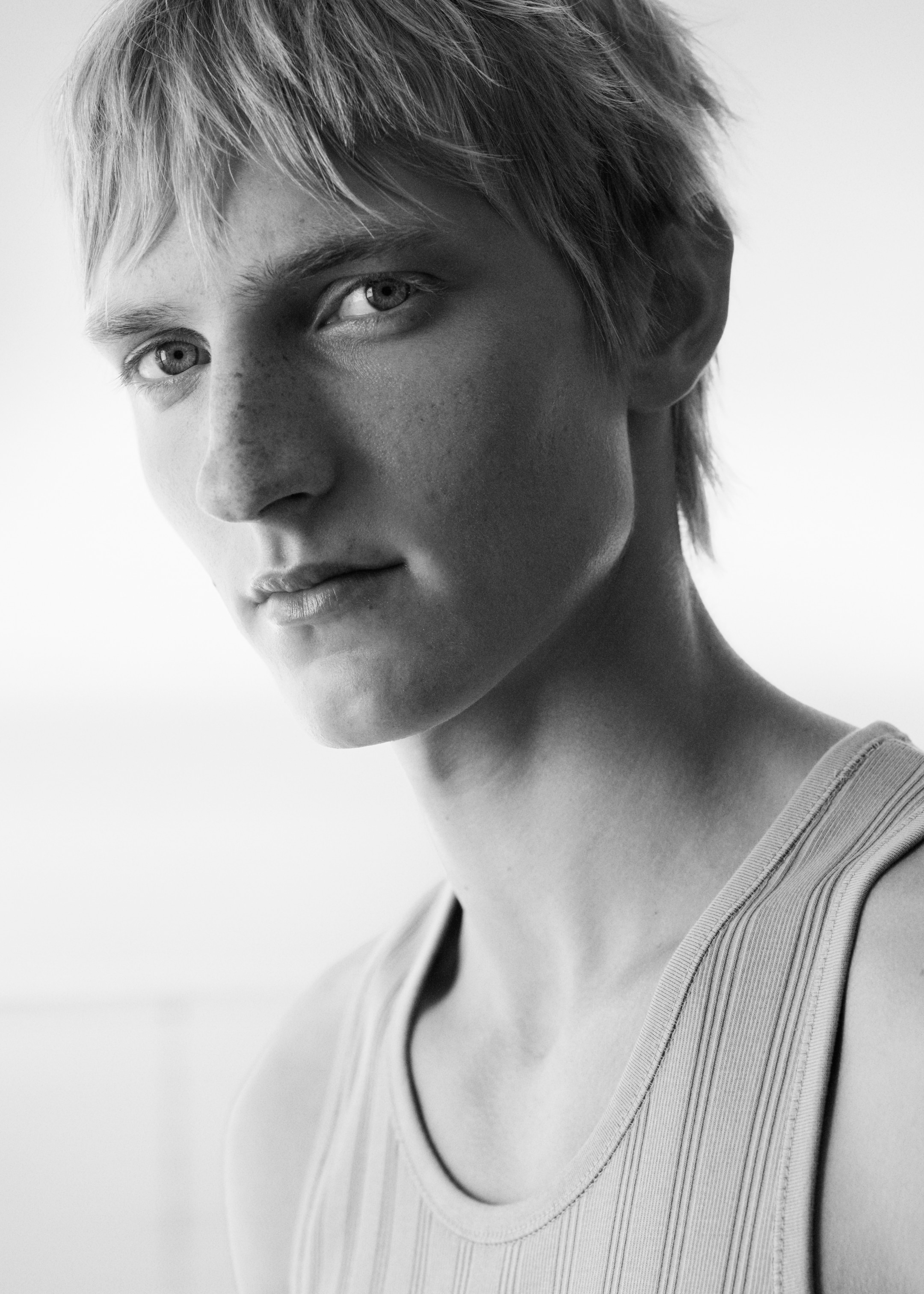 Black and white portrait of a young person with short hair, wearing a sleeveless top, gazing slightly away from the camera.