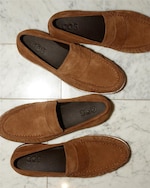 Placeholder for: Two pairs of brown suede loafers with "COS" insoles are placed on a white marble floor.