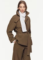 Placeholder for: Woman looking at camera with tan funnel neck coat and white blouse