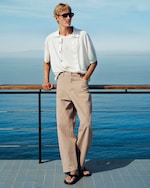 Placeholder for: person standing wearing a white knitted linen shirt over a white t-shirt and beige denim trousers