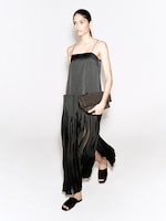 Placeholder for: A woman in a sleek black dress with thin straps and a fringe skirt holds a textured clutch. She walks confidently, wearing black open-toe sandals.