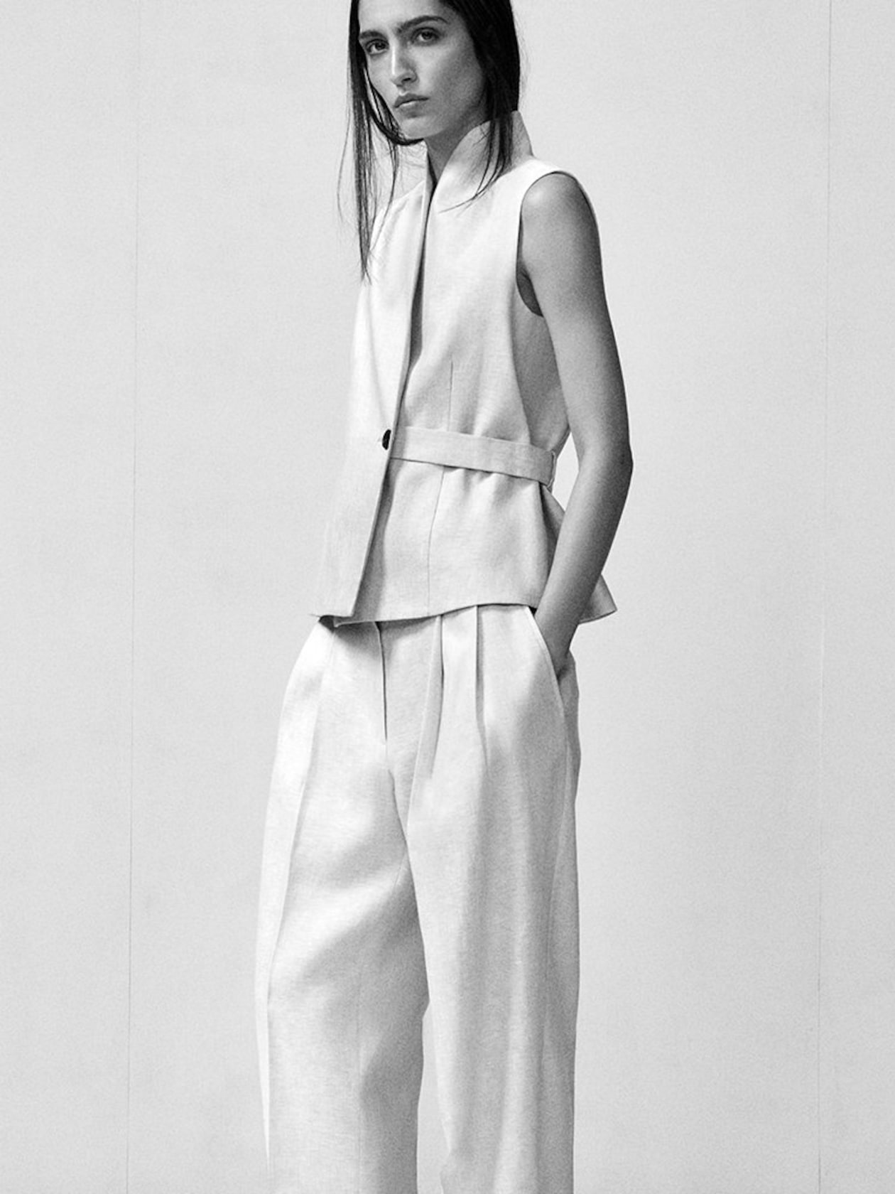 A person wearing a tailored sleeveless top and wide-legged pants in a minimalist setting.