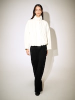 Placeholder for: A person wearing a white jacket and black pants walks confidently, casting a shadow on a light background.