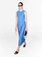 Placeholder for: A person wearing sunglasses and a sleeveless blue dress walks while holding a black clutch, sporting black slide sandals.