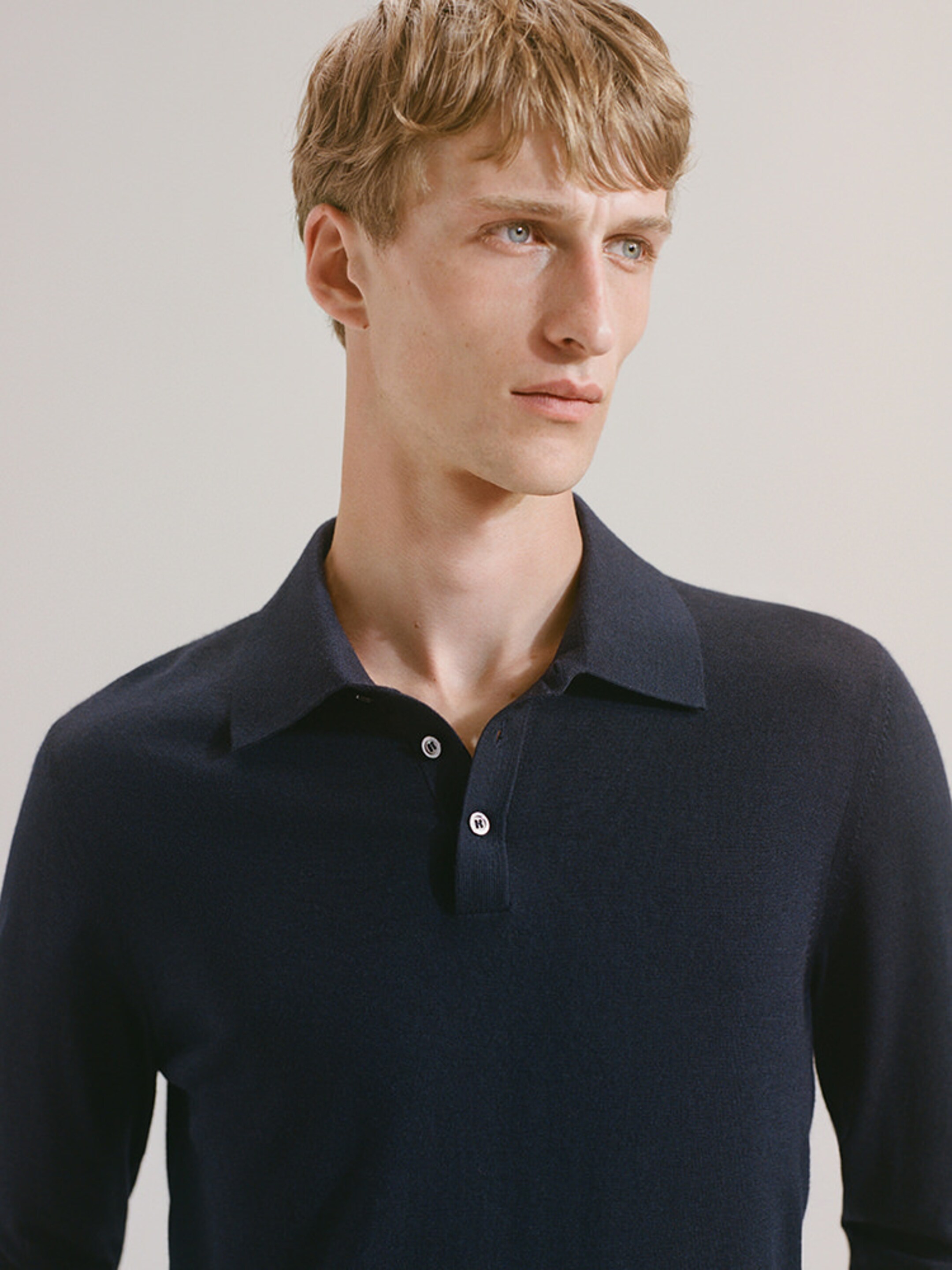 Person wearing a navy collared shirt, looking to the side against a neutral background.